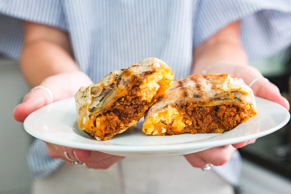 a person holding a burrito on a plate