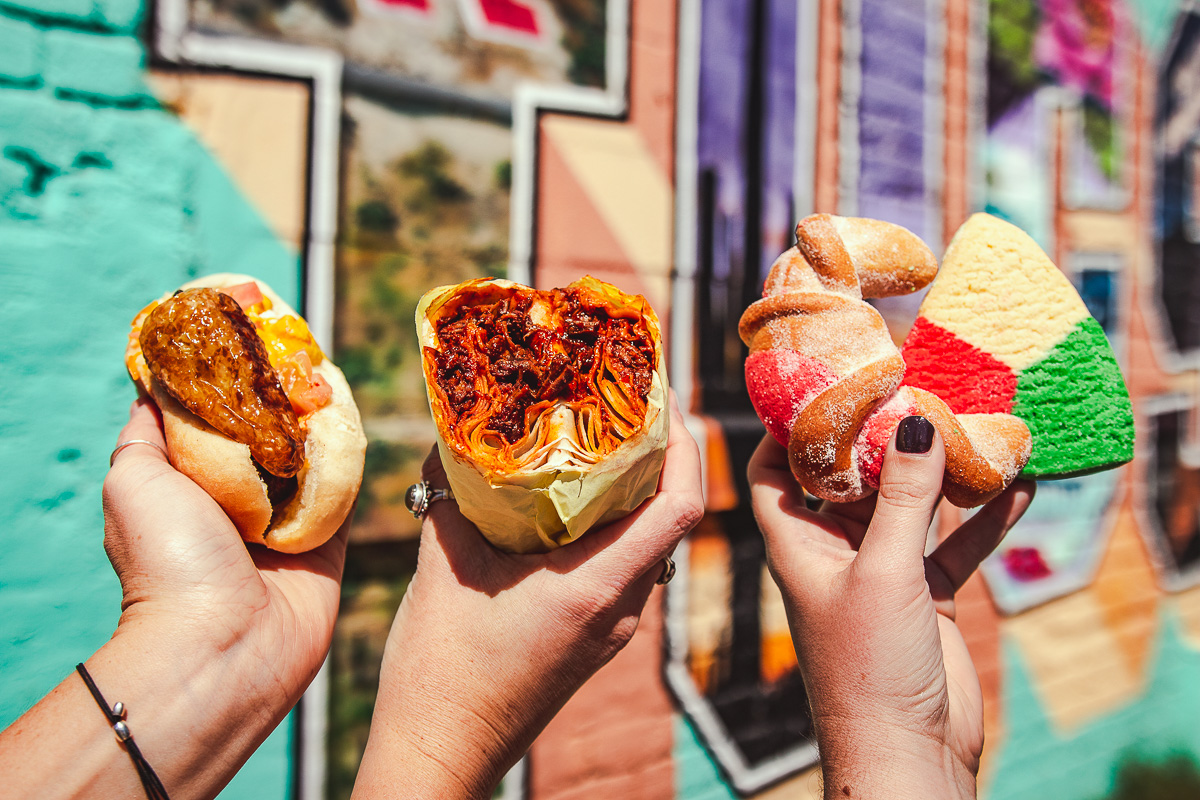 Sonoran hot dog, red chile burro, and pan dulce from Anita Street Market in front of the Greetings from Tucson Mural (Credit: Jackie Tran)